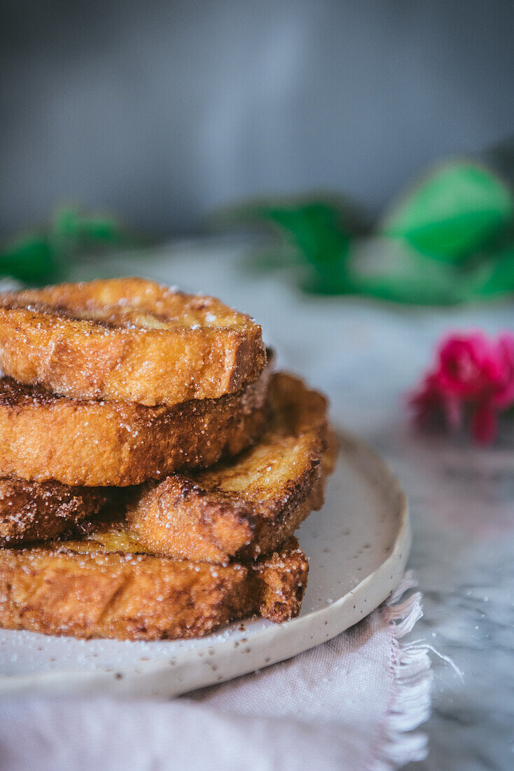 Homemade traditional easter Spanish French toast dessert served on plate near a rose flower on marple background