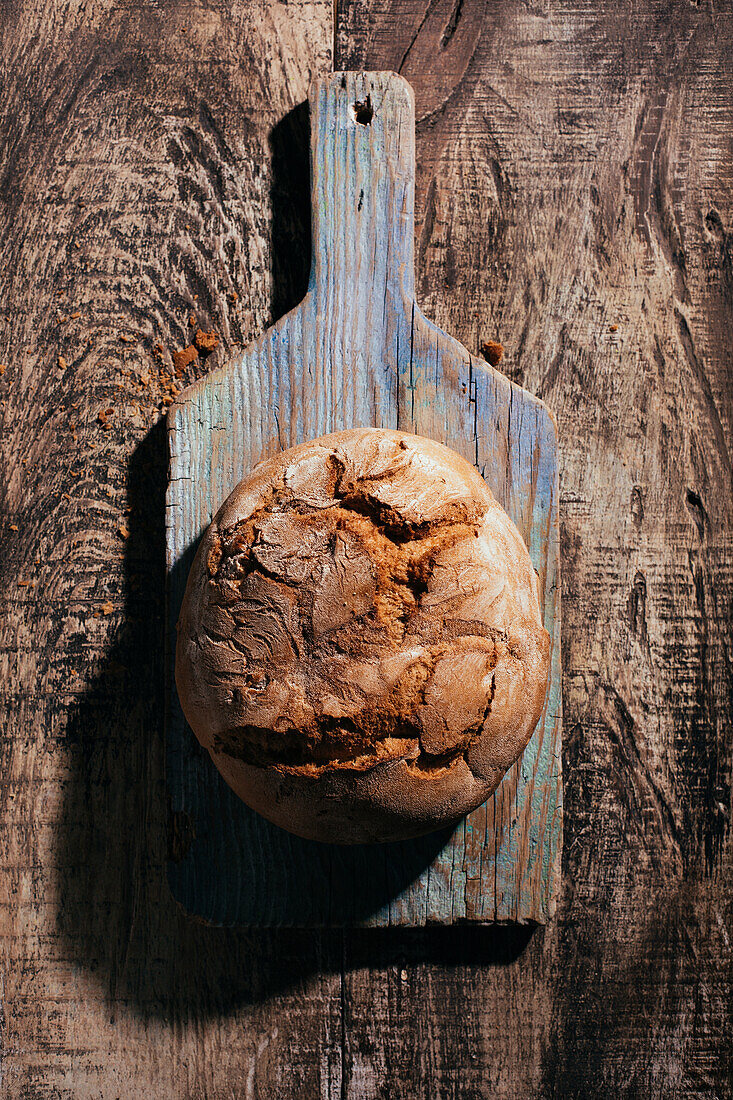 Draufsicht auf ein köstliches, frisch gebackenes Brot auf einem alten Schneidebrett auf einem Holztisch in der Küche