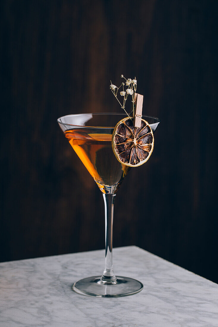 Glas eines traditionellen alkoholischen Manhattan-Cocktails, garniert mit einer Orangenscheibe und Blumen auf dem Tisch