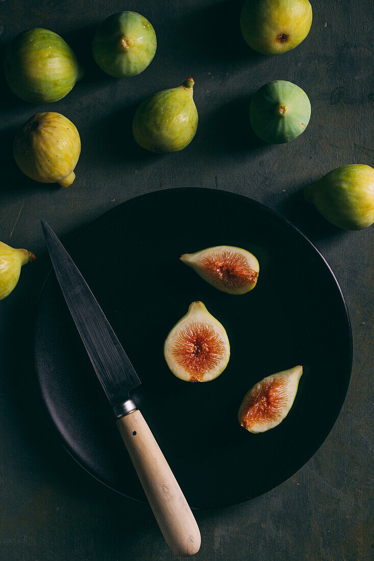 Top view of fresh sweet figs arranged on plate with knife on dark background