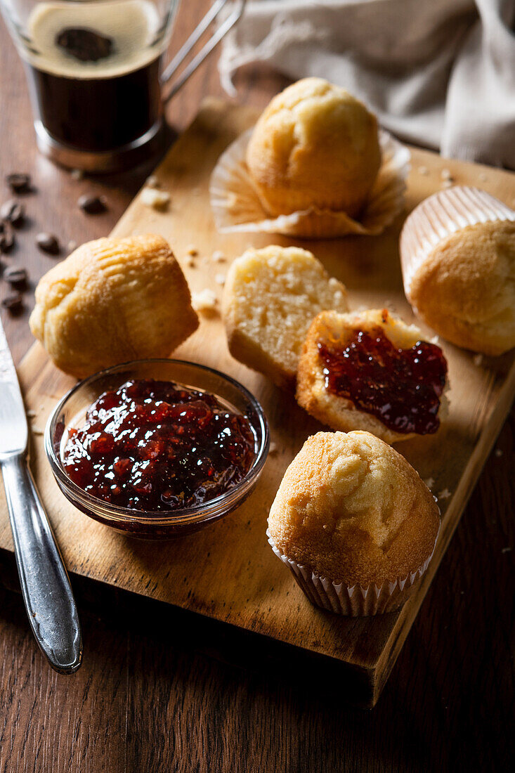 From above delicious homemade muffins and raspberry jam on wooden board near coffee on table