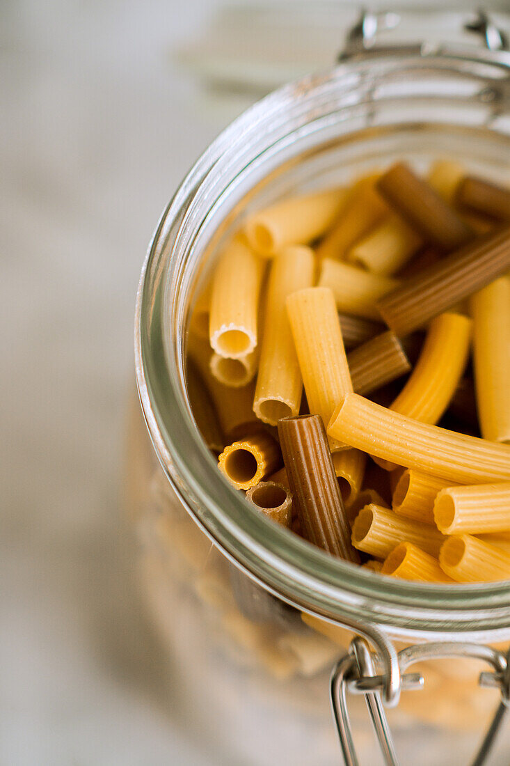 Closeup glass jar filled with different colored pasta on table