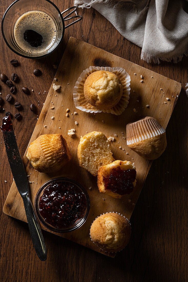 From above delicious homemade muffins and raspberry jam on wooden board near coffee on table