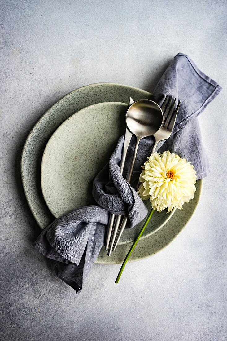 From above plates setting with white Dahlia flower on concrete table