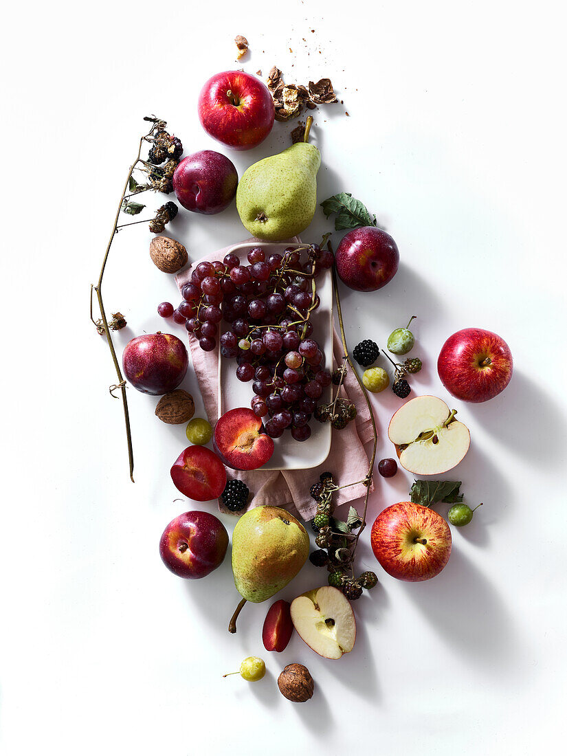 Composition with fresh summer fruits and berries on white background. Grapes, plums and apples in sunlight.