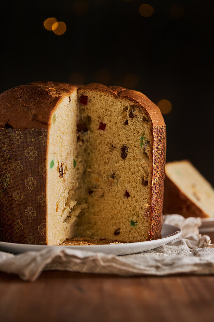 In Scheiben geschnittener, frisch gebackener, handwerklich hergestellter Weihnachts-Panettone-Kuchen unter warmem Licht vor Bokeh-Hintergrund