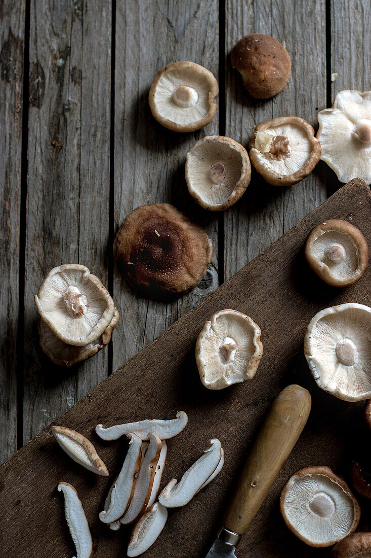 Blick von oben auf ein Holzbrett mit einer Schüssel voller Shiitake-Pilze und Auberginen darauf