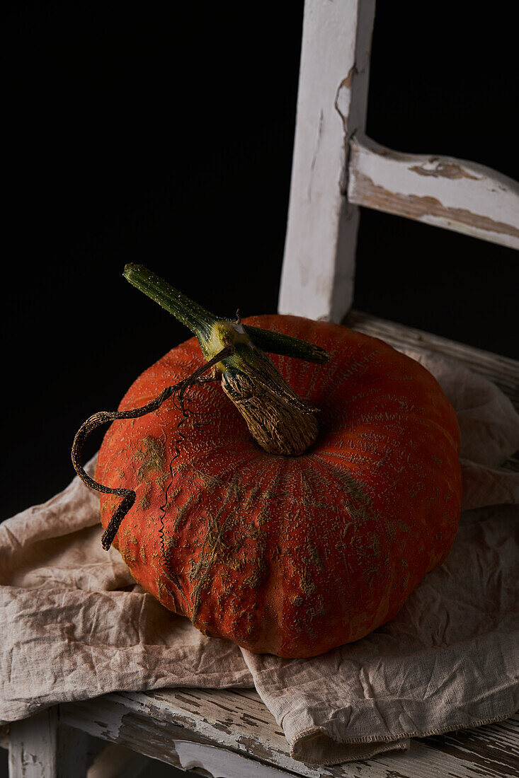 From above whole ripe pumpkin with slightly ribbed skin placed on wooden white chair against black background