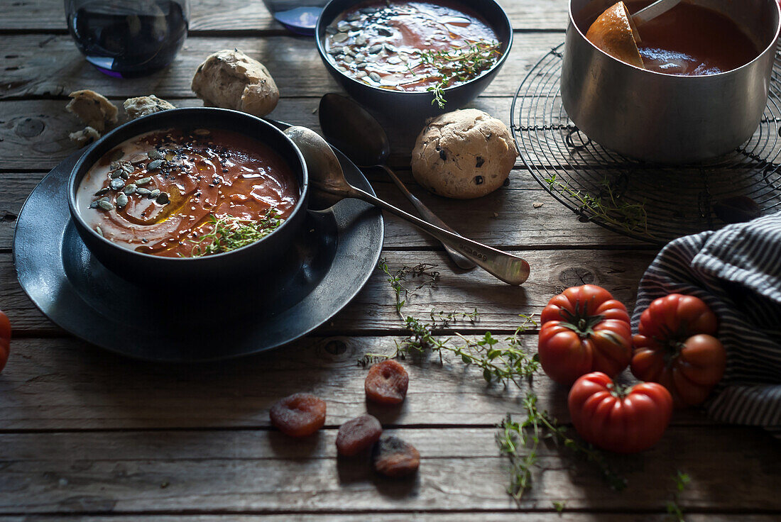 Komposition aus servierten Schalen mit köstlicher Tomatencremesuppe mit Kernen auf einem Tisch mit Tomaten und Brotbrötchen