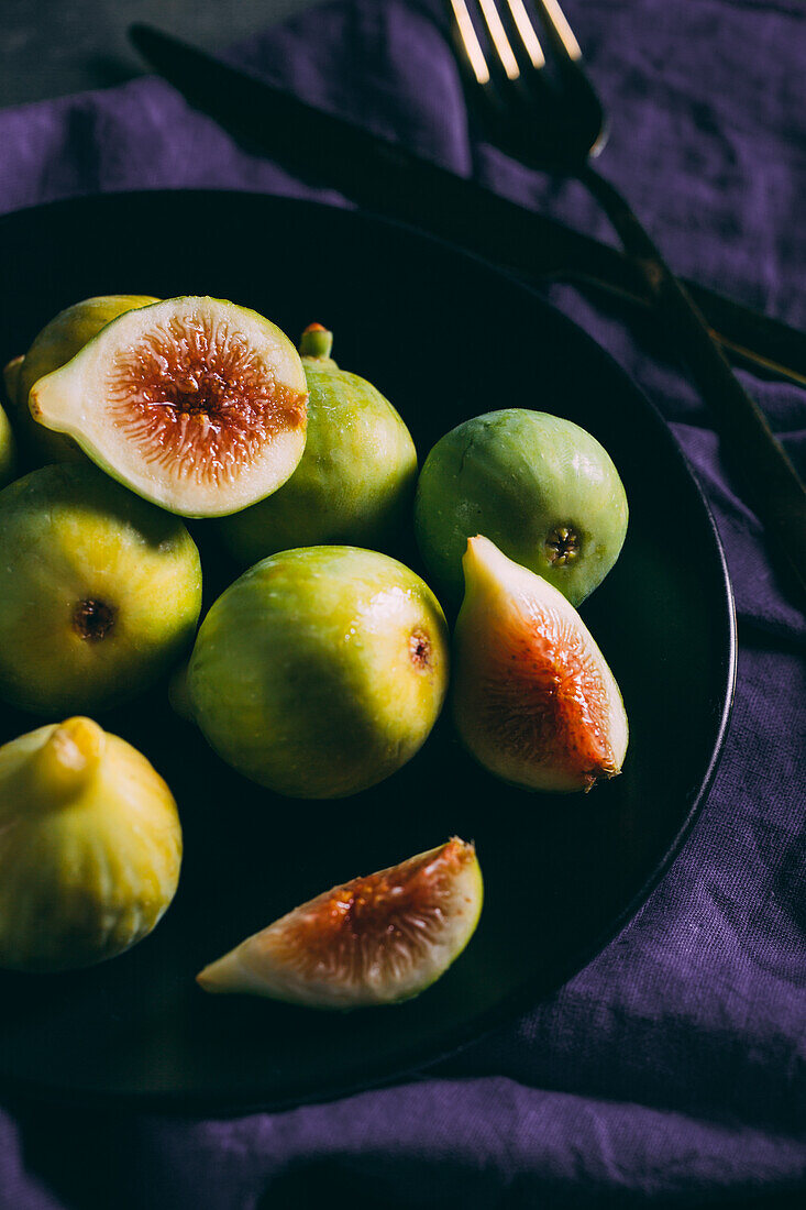 Top view of fresh sweet figs arranged on plate with fabric napkin on dark background