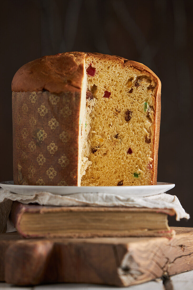 Still life of sliced fresh baked artisan Christmas panettone cake on vintage book and cutting board against dark background