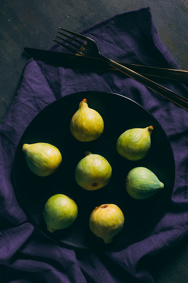 Top view of fresh sweet figs arranged on plate with fabric napkin on dark background