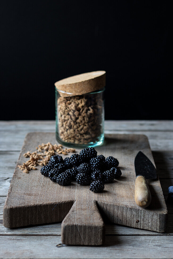 From above view of glass jar full of walnut granola and pile of blueberries placed on wooden cutting board on black background