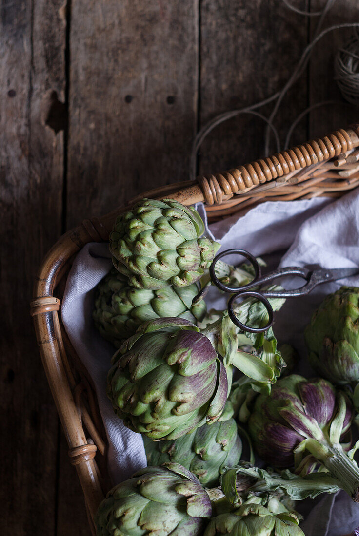 Closeup from above view of green artichokes laid in wicker basket with bunch of little purple flowers