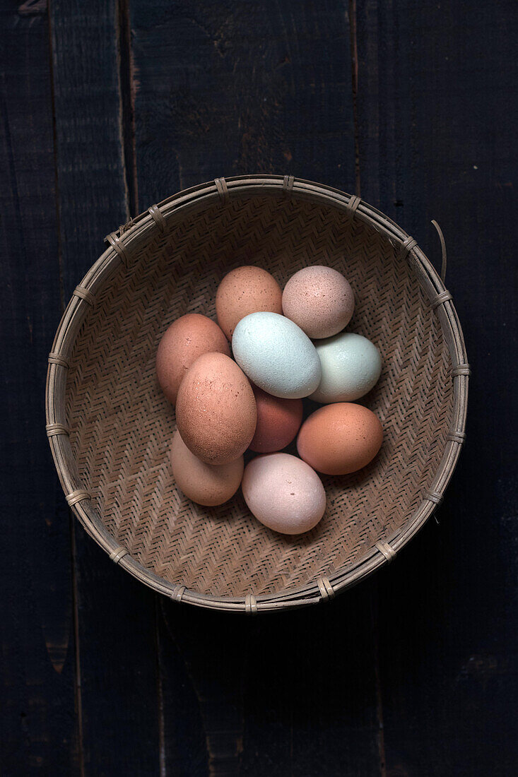 Blick von oben auf einen mit braunen und weißen Eiern gefüllten Weidenkorb auf einem Tisch