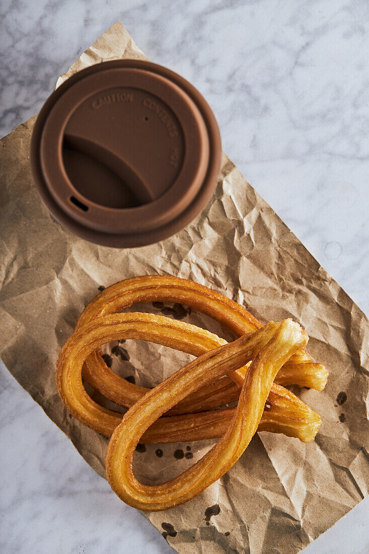 Fresh crispy churros and cup of hot coffee placed on table for breakfast
