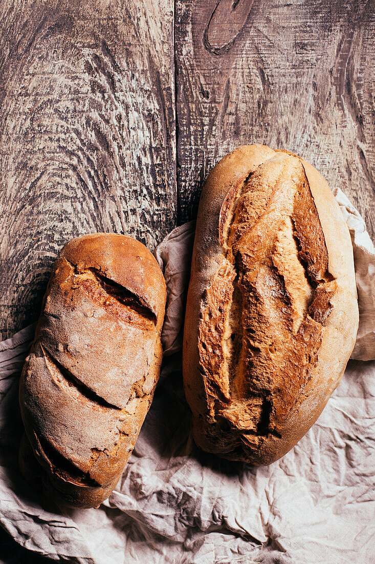 Top view of freshly baked delicious sourdough breads of various shapes placed on wooden table in bakery