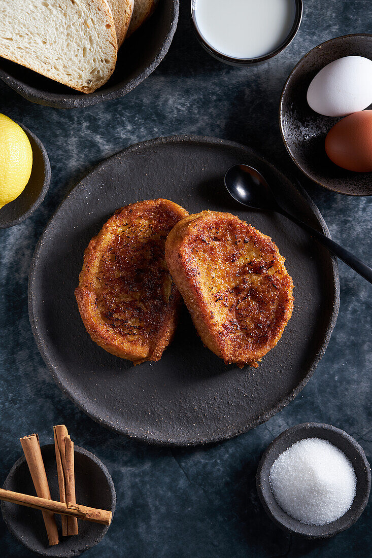 High angle plate of freshly prepared yummy torrija arranged with bowls of milk and eggs placed on table in kitchen