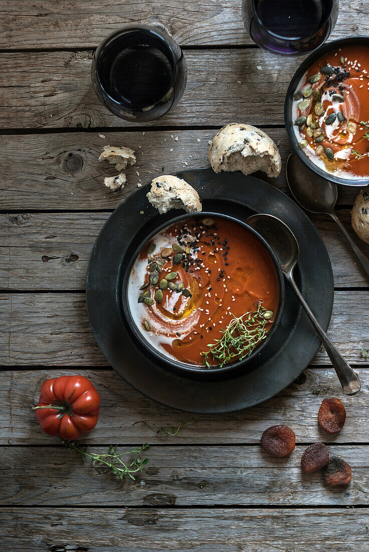 Flat lay of bowls with creamy tomato soup garnished with seeds and served on table with tomatoes and dried apricots