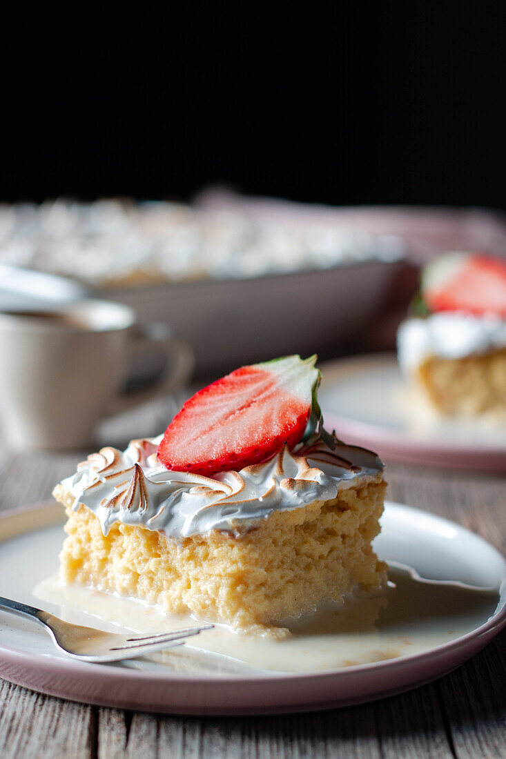 Sweet delicious piece of three milks cake with half fresh strawberry on white plate on wooden table