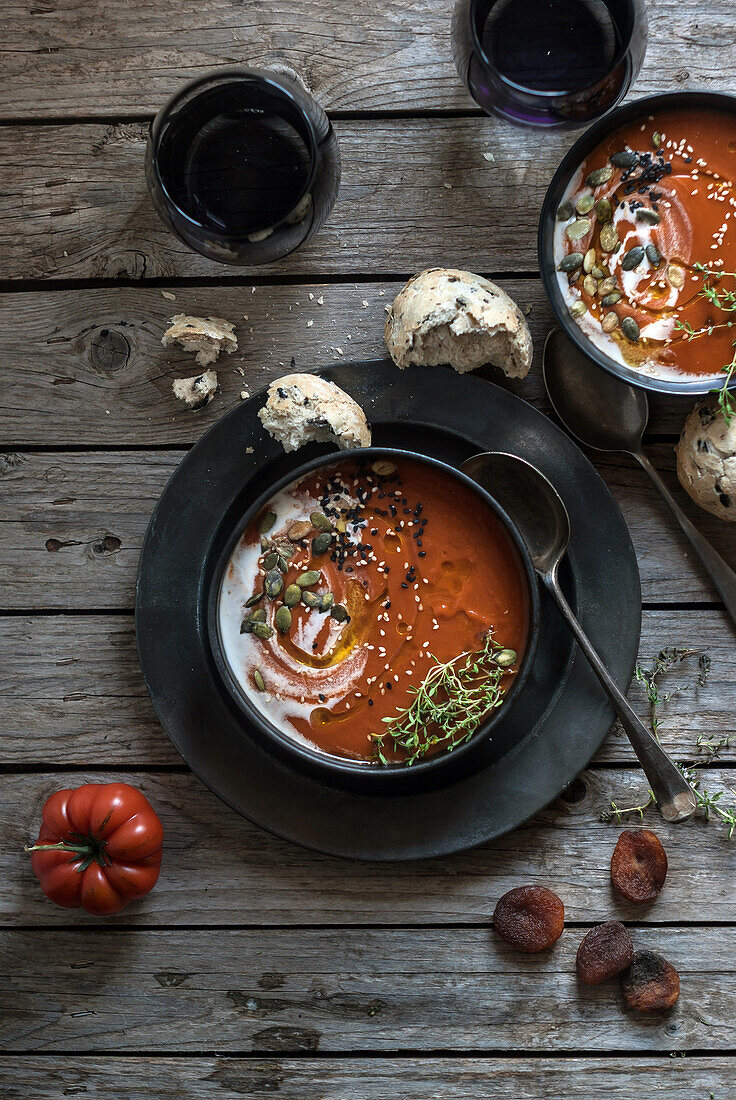 Komposition aus servierten Schalen mit köstlicher Tomatencremesuppe mit Kernen auf einem Tisch mit Tomaten und Brotbrötchen