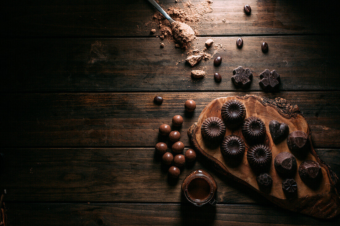 Leckere handgemachte Pralinen auf einem Schneidebrett in der Nähe eines Mousse-Glases in der Küche (von oben)