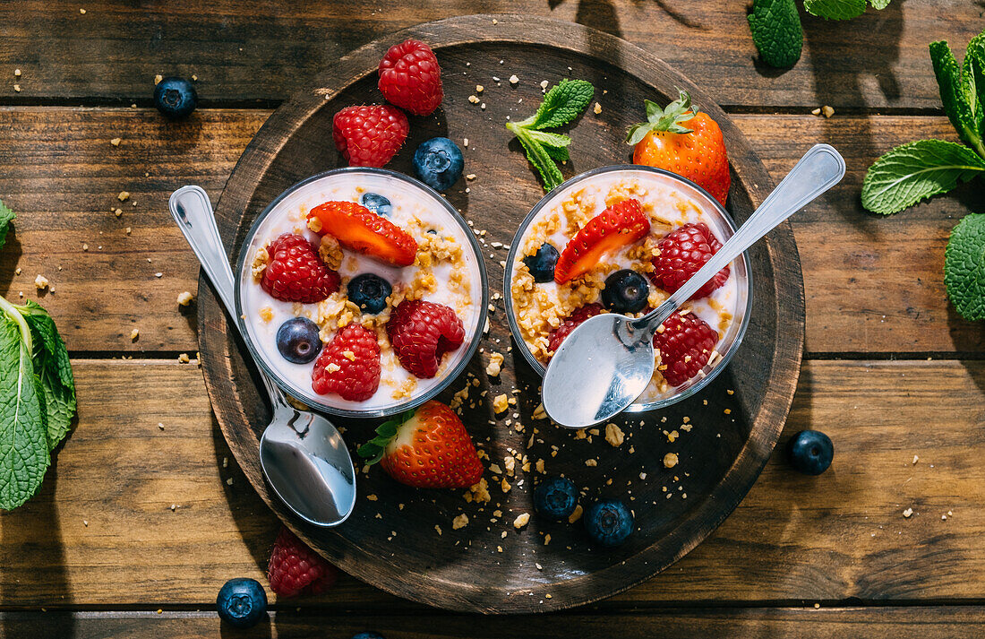 Blick von oben auf köstlichen hausgemachten Joghurt mit Erdbeeren, Beeren und Müsli auf Holztisch Hintergrund