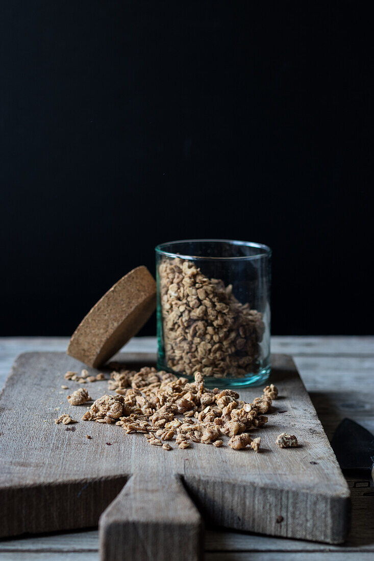 Glass jar with walnut granola laid on wooden chopping board on black background
