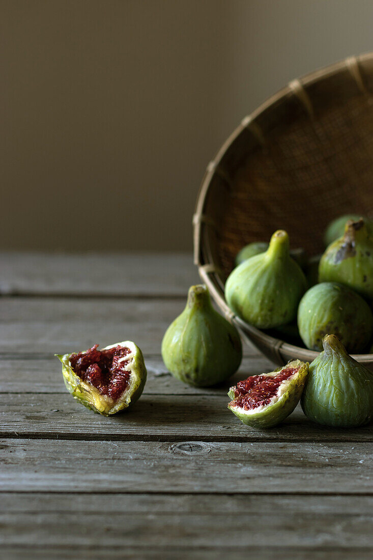 Nahaufnahme eines Korbes mit grünen Feigen und geteilten Früchten mit rotem Fruchtfleisch auf einem Tisch