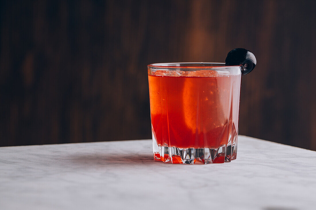 Glas alkoholischer roter Bloody-Mary-Cocktail mit Eiswürfeln, garniert mit schwarzer Olive, auf dem Tisch serviert