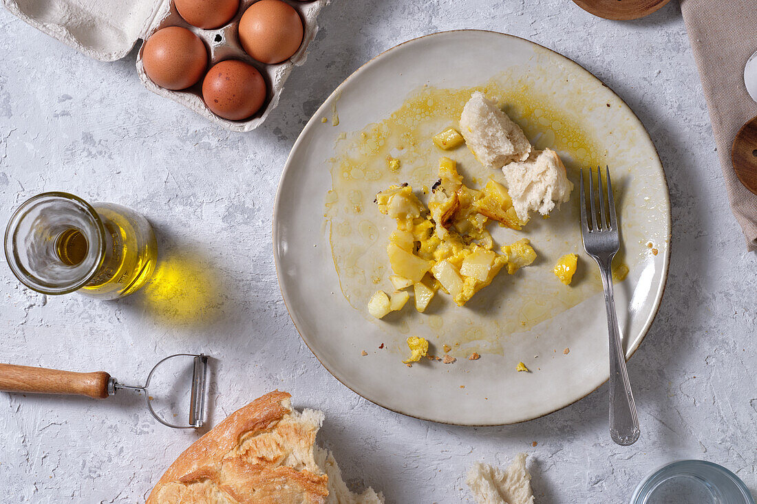 Top view of dirty plate with leftovers of Spanish omelette and bread placed on table in kitchen