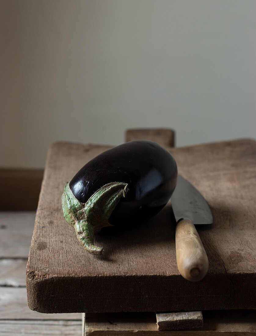 Fresh ripe eggplant with knife laid on wooden chopping board on box