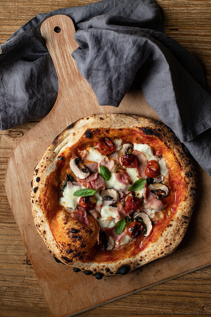 Top view of delicious pizza with basil and tomato sauce placed on wooden table near napkin in kitchen