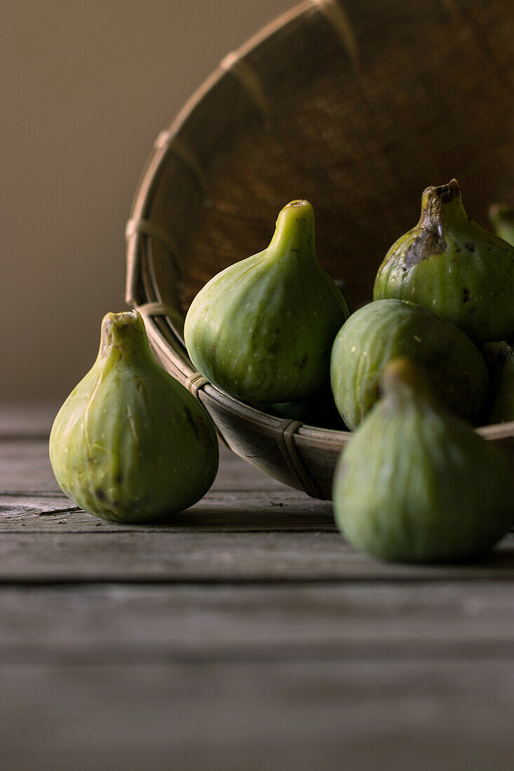 Closeup of round wicker bowl full of green figs lying on wooden table