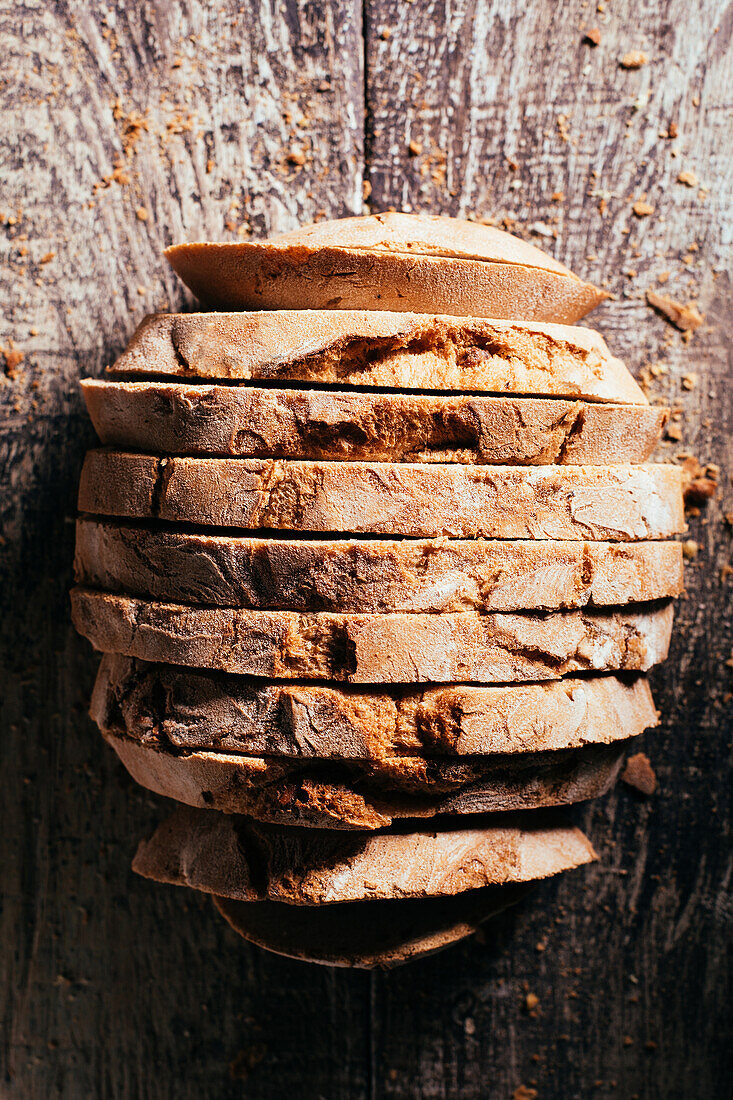 Köstliches frisch gebackenes Brot auf altem Schneidebrett auf einem Holztisch in der Küche von oben