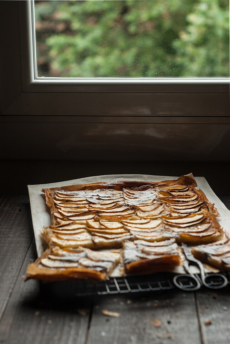 Köstlicher Bratapfelkuchen mit Frangipane, in Stücke geschnitten und auf einem Kühlregal am Fenster angerichtet