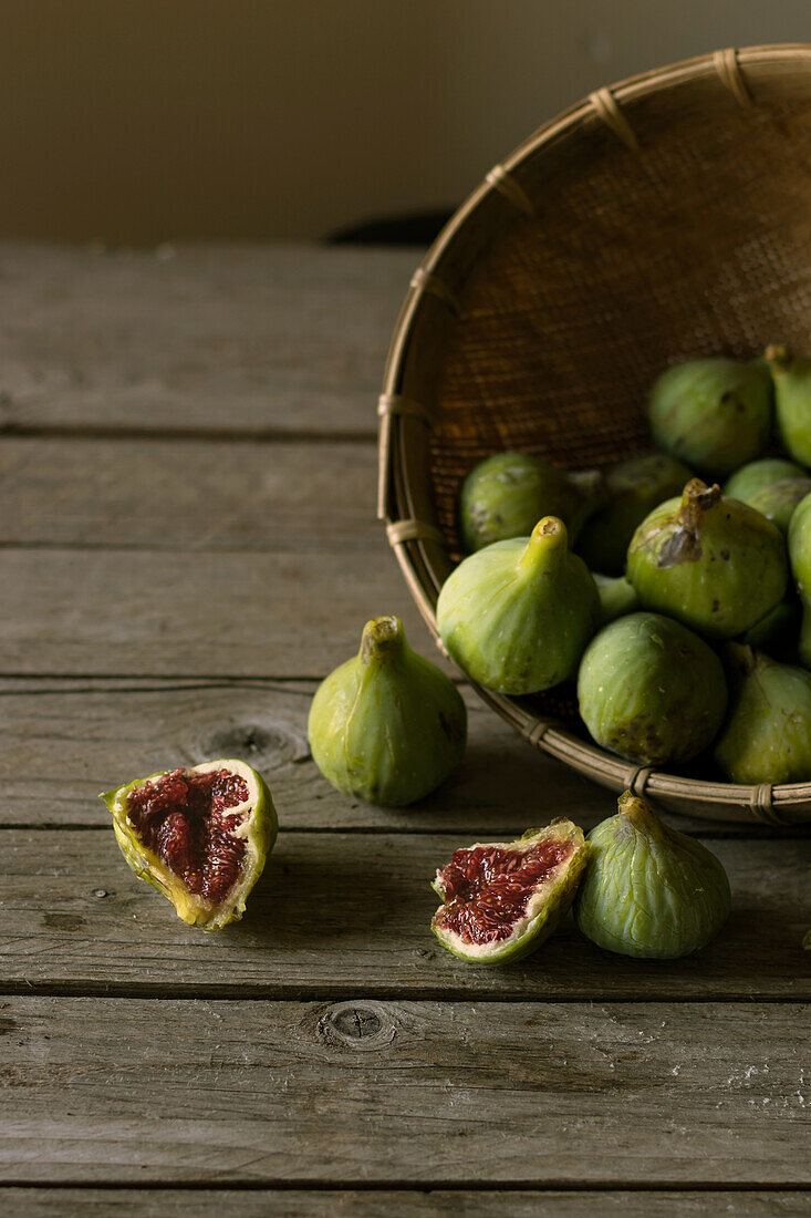 Closeup shot of basket with green figs and split fruit with red flesh on table