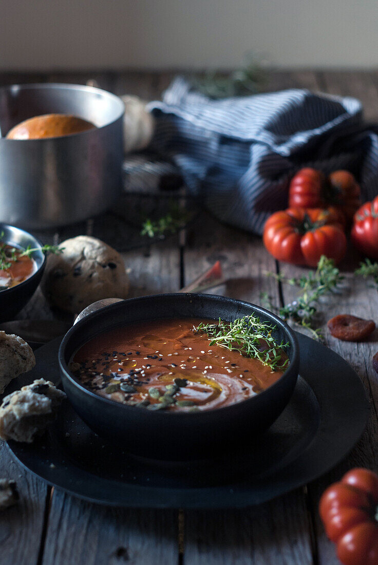 Composition of served bowls with delicious tomato creamy soup with seeds on table with tomatoes and bread buns