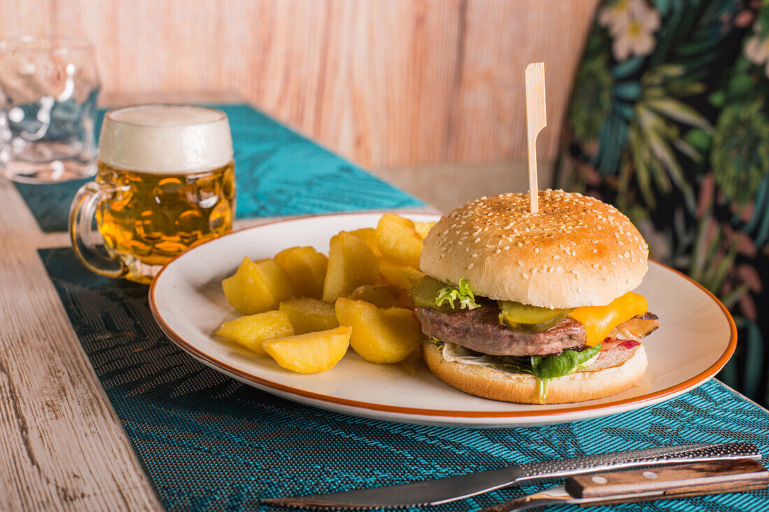 Leckerer Burger und Kartoffeln auf einem Teller, serviert auf einem Tisch mit einem Glas frischem Bier in einem Cafe