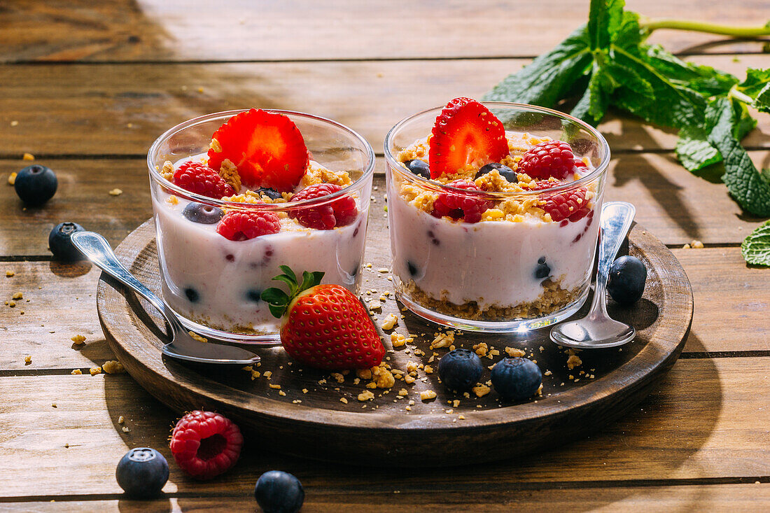 Köstlicher hausgemachter Joghurt mit Erdbeeren, Beeren und Müsli auf einem Holztisch im Hintergrund