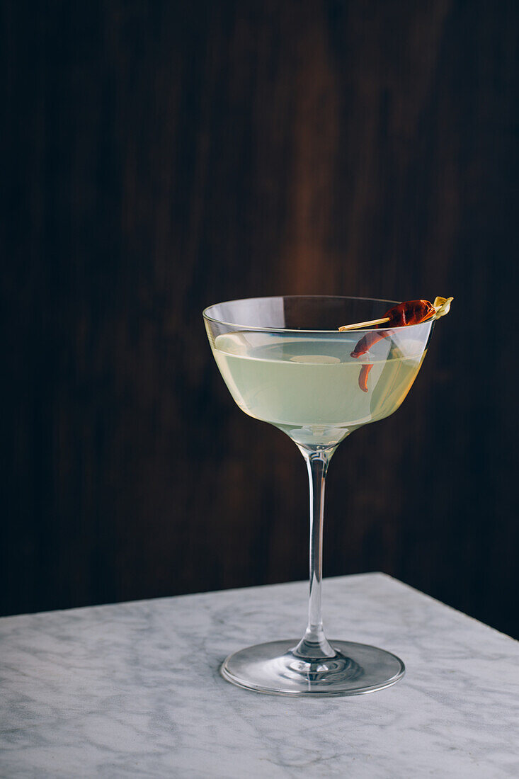 Glass goblet of martini cocktail garnished with red pepper served on table against black background