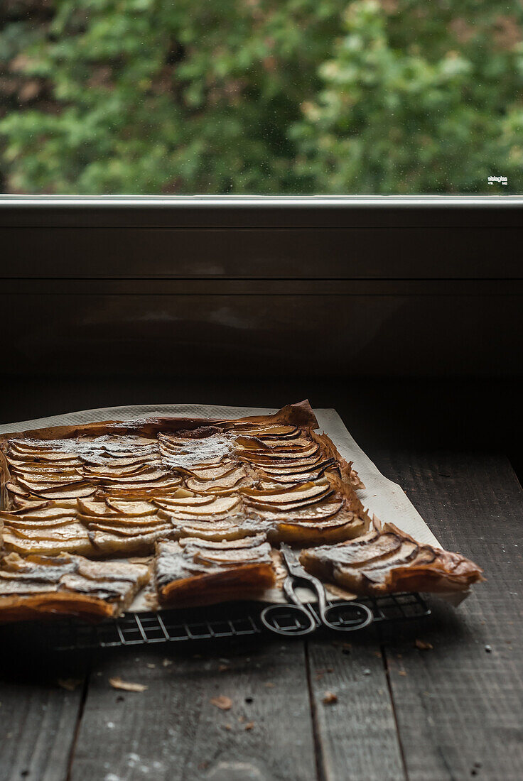Delicious baked apple pie with frangipane cut into pieces and composed on cooling rack near window