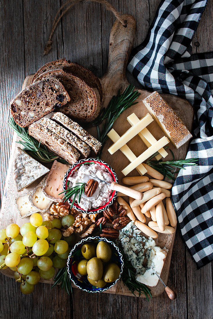 Von oben verschiedene Käsesorten mit Brot, Oliven und Trauben auf Käseplatte auf Holztisch