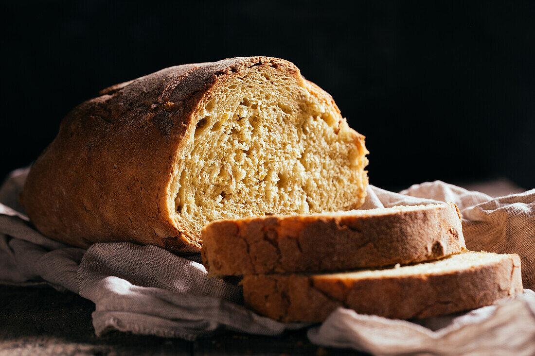 Freshly baked cut bread loaf placed on wooden table in kitchen on sunny day