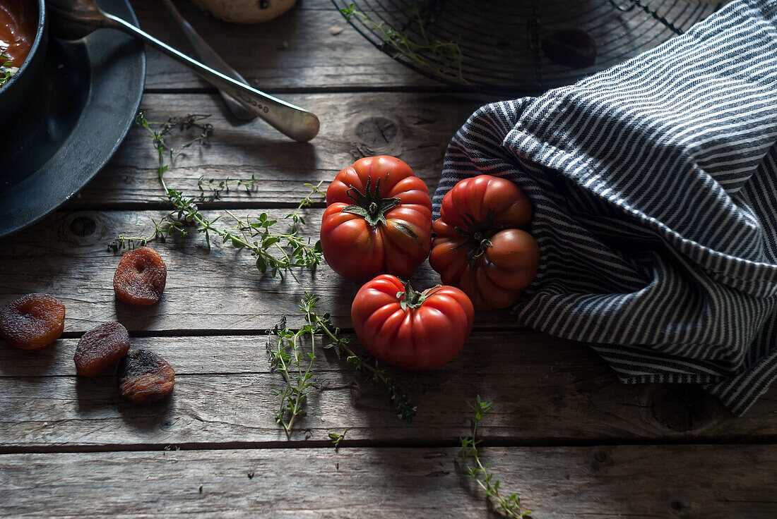 Draufsicht auf einen Holztisch mit einem Haufen reifer roter Tomaten und getrockneter Aprikosen bei Tageslicht