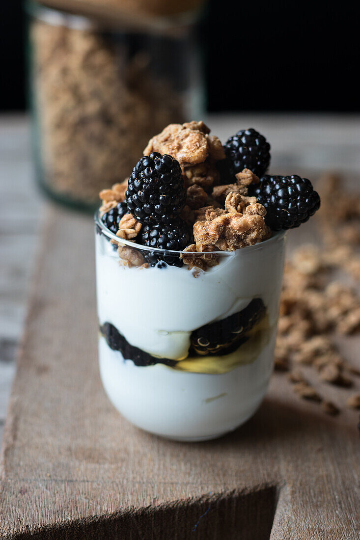 Nahaufnahme von oben eines Glases mit Walnuss-Müsli, gemischt mit Blaubeeren und Joghurt, das auf einem hölzernen Schneidebrett neben dem Glas steht