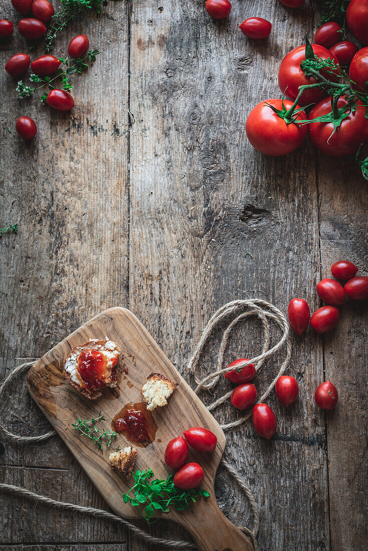 Top view of chopping board with bread and herbs placed near tomato jam on lumber table in rustic kitchen