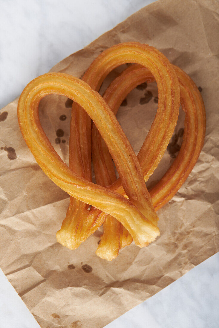 Blick von oben auf knusprige Churros, die auf Papier auf einem weißen Tisch im Studio serviert werden