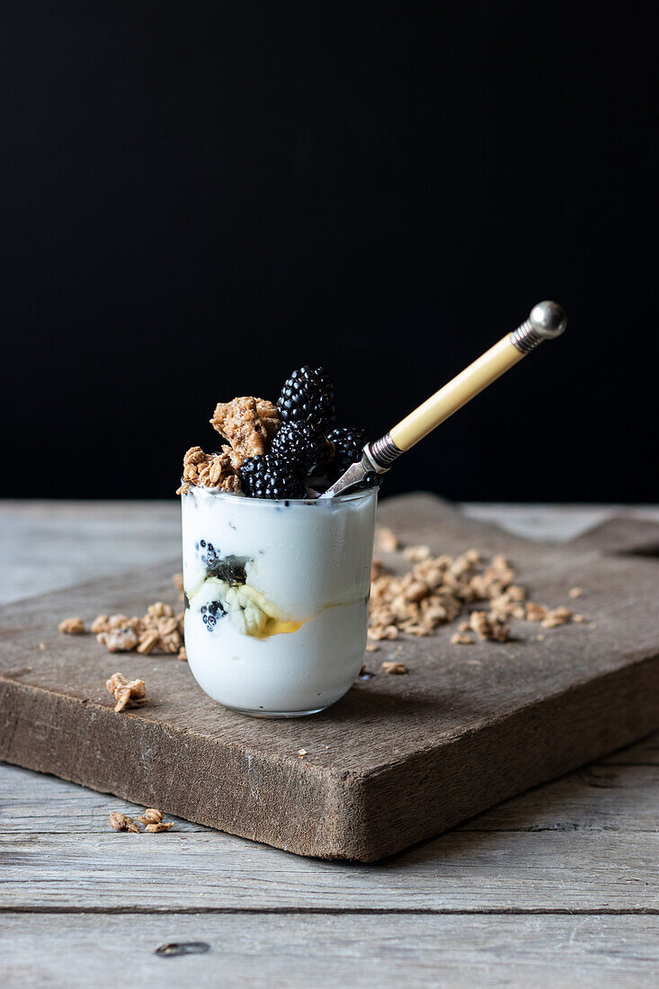 Closeup from above view of glass with walnut granola mixed with blueberries and yogurt placed on wooden chopping board near jar