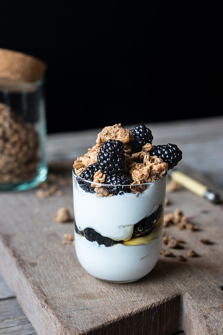 Closeup from above view of glass with walnut granola mixed with blueberries and yogurt placed on wooden chopping board near jar